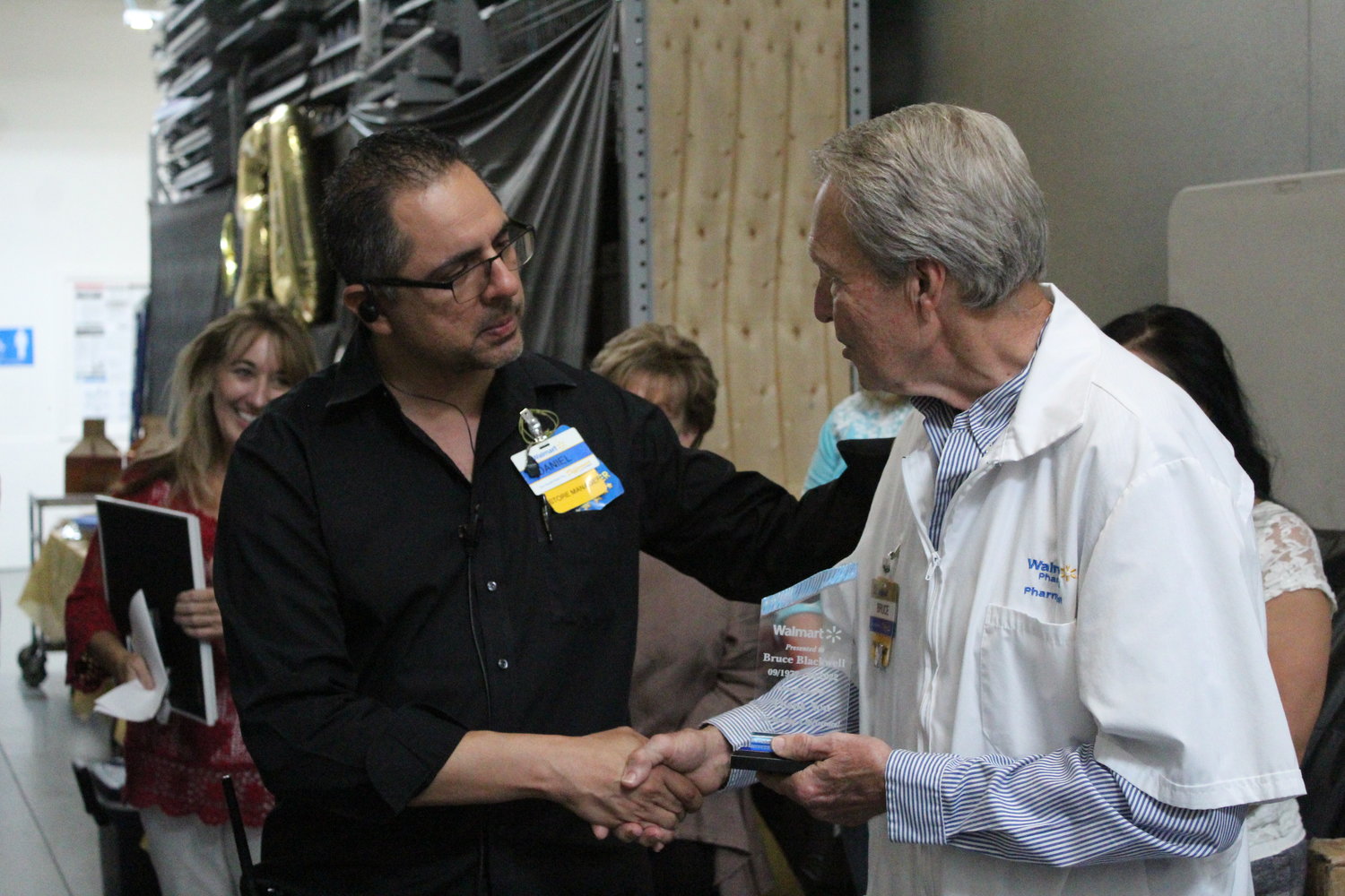 Gonzales Walmart store manager Daniel Trevino (left) shakes hands with Walmart’s Pharmacist Manager Bruce Blackwell (right) as he congratulates him for 50 years of working with the company.